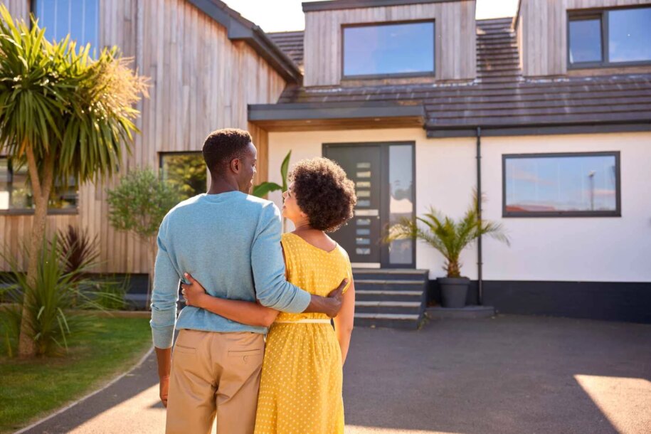 Rear view of couple standing in driveway in front of their real estate property